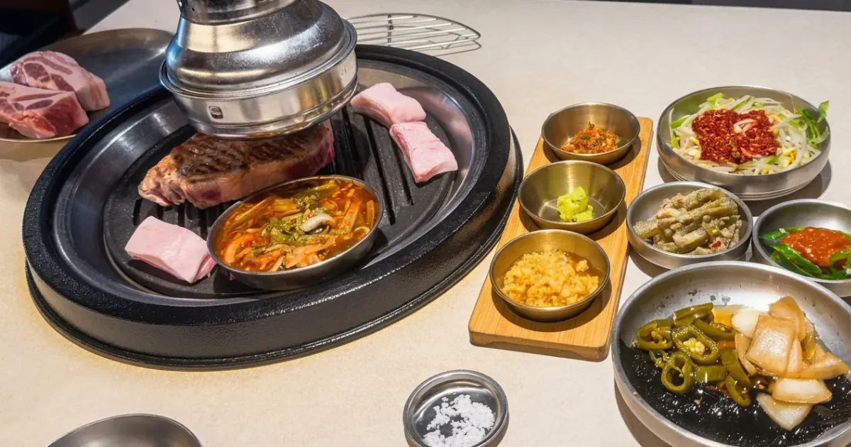 Pork cuts on the grill and side dishes with wasabi, minced garlic, and pickles at BBQ Yul, a Korean BBQ restaurant in Seoul